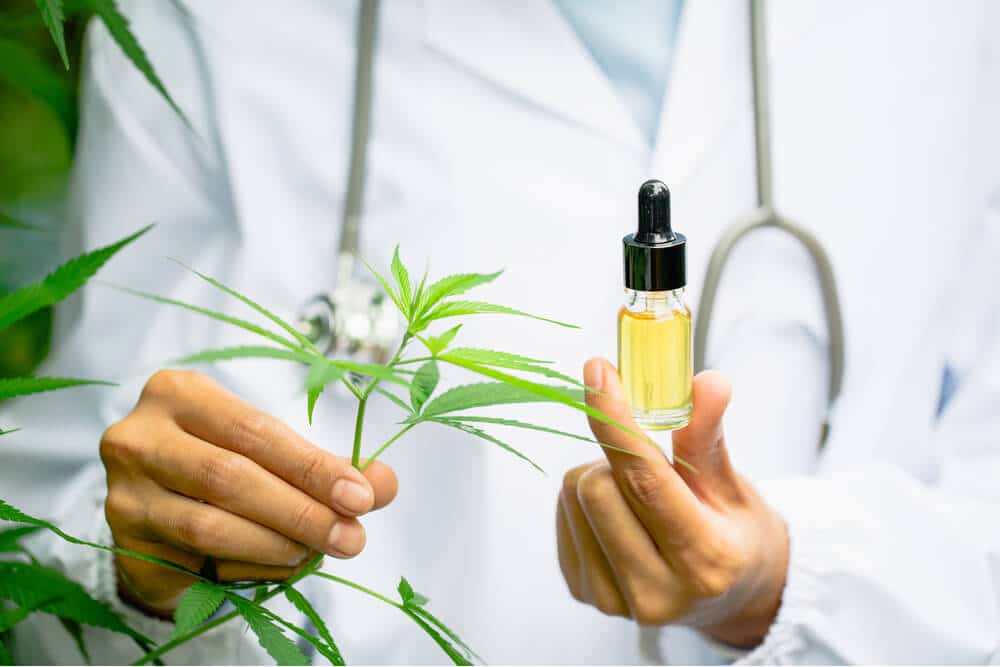 Person in lab coat holding CBD oil dropper