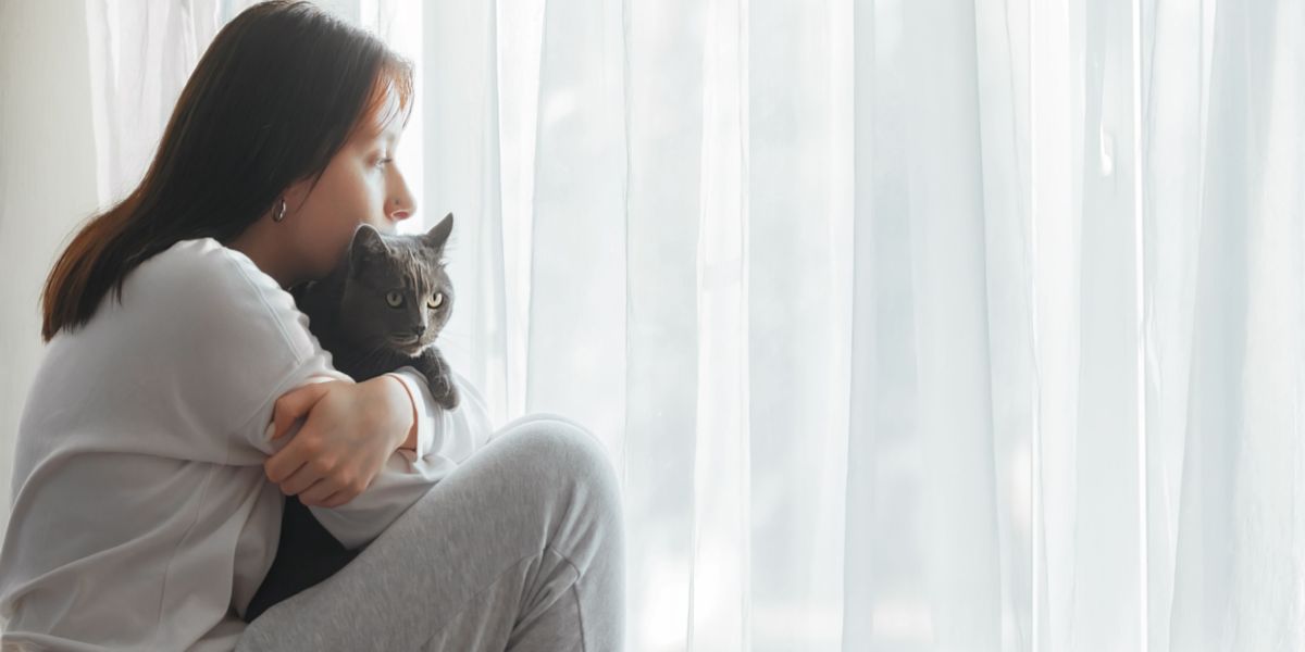 Image of a woman looking sad while sitting with a cat, possibly indicating a moment of comfort or support.