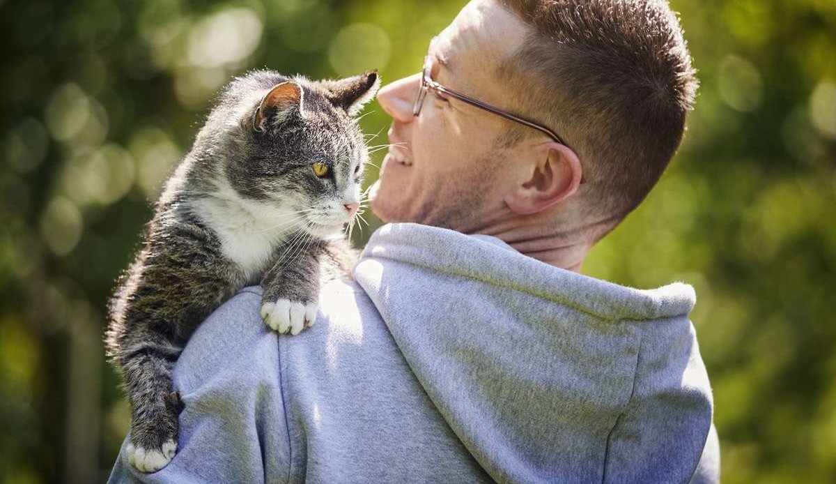 Smiling man carrying his senior tabby cat in the garden